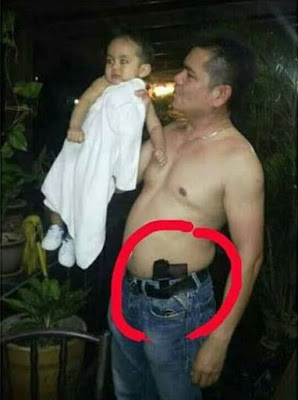 Jamal menjulang seorang bayi sambil pistol tersisip dipinggang